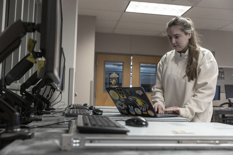 photo of female student on a laptop in a classroom with a computer lab.
