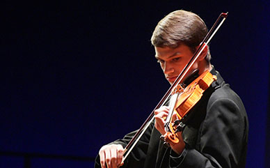 photo of male LCCC student playing a donated violin during a concert. He's standing doing a solo.