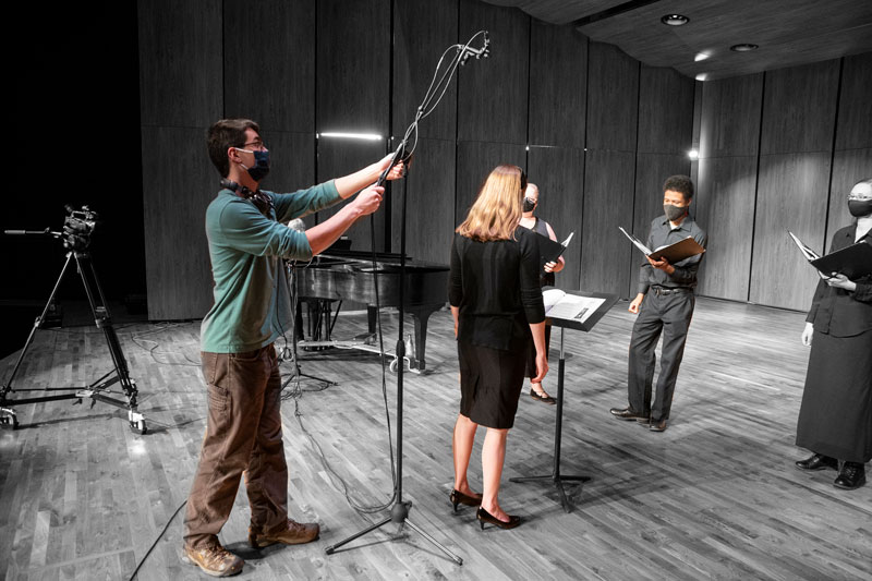 Student holding a microphone over musicians while recording for a virtual concert