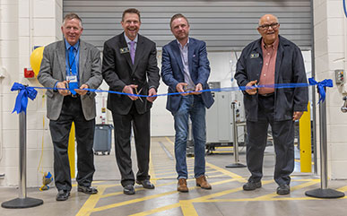 photo of the ribbon cutting for the AMMC with four men cutting a ribbon in the new space