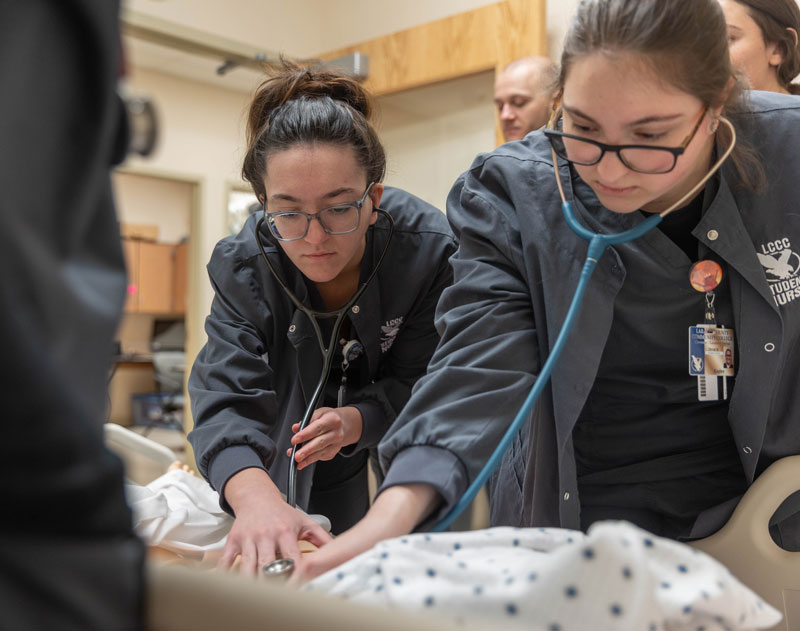 nursing students listen to a heart beat on a training SIM