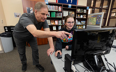 Leland Weber talking with a student working on a computer