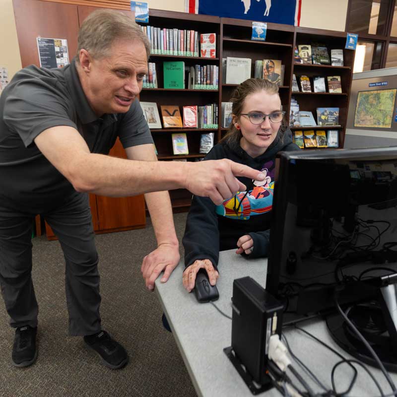 Leland Weber talking with a student while they work on a computer