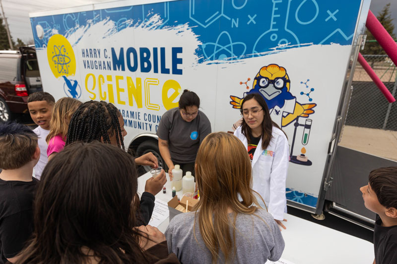 Photo of an LCCC student in front of the mobile science lab with elementary age students talking