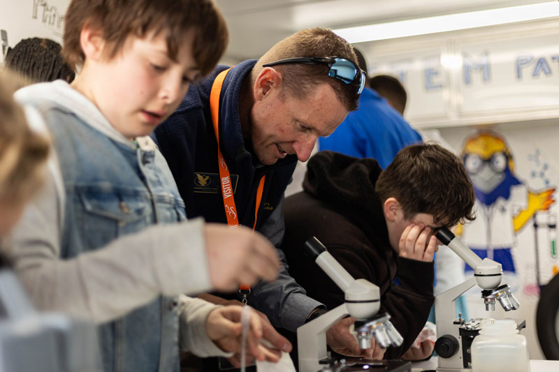 Photo of an LCCC faculty and elementary age students looking in microscopes inside the mobile science lab