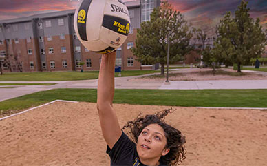 Photo of a student athlete hitting a volleyball at the sand volleyball court outside on campus