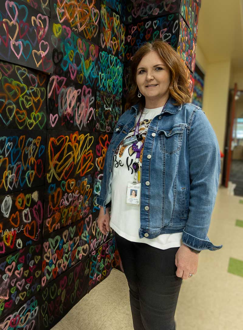 Lindsey Belmonte standing in front of heart artwork at school