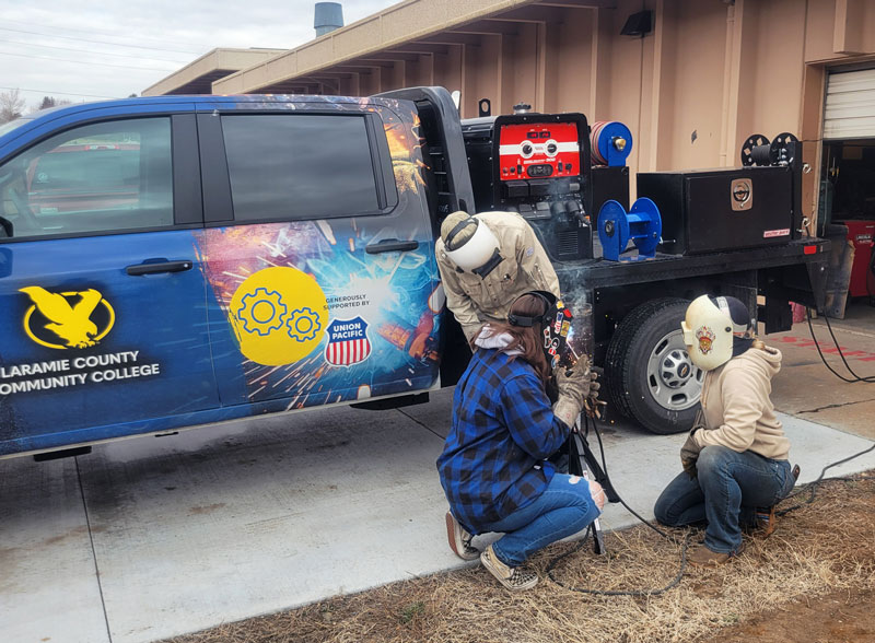 Photo of an LCCC students in front of the mobile welding truck welding with masks on 