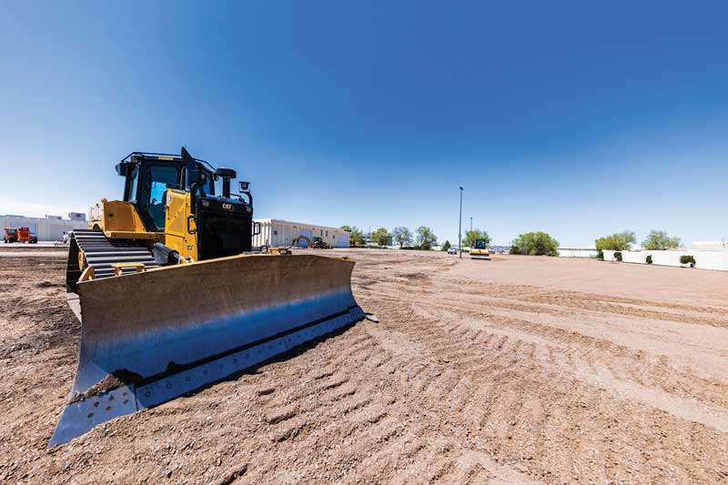 A tractor working in a dirt parking lot on campus. The concrete has been removed.