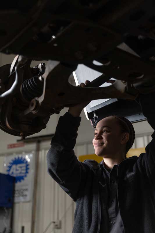 Jaya Brown standing under a car in the Auto Tech bay working on the underside