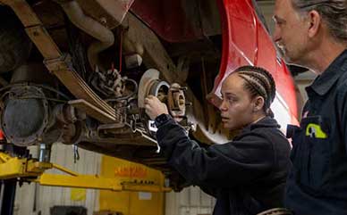 Jaya working on a car wheel in class with an instructor nearby