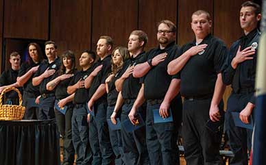 A line of Emergency Medical Services students with the hands over their hearts on stage during the EMS coining ceremony