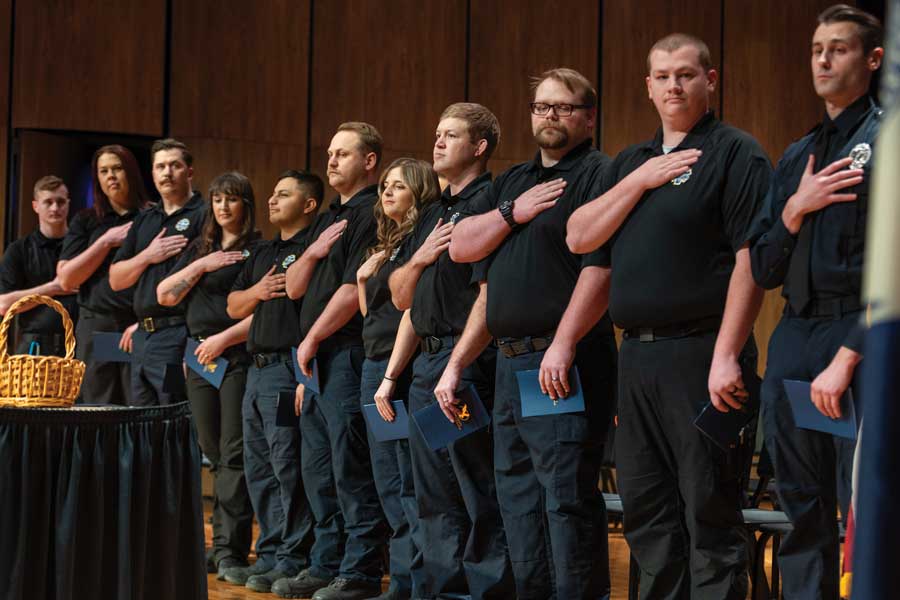 A line of Emergency Medical Services students with the hands over their hearts on stage during the EMS coining ceremony