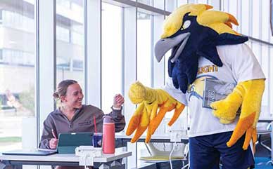 a student sitting at a table in the library fist pumping the LCCC Talon mascot