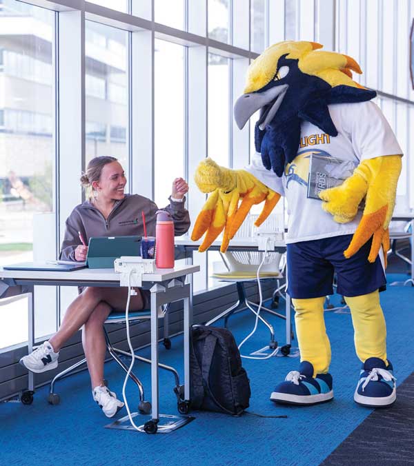 a student in the library at a table with notes and a water bottle fist bumping Talon, the LCCC mascot