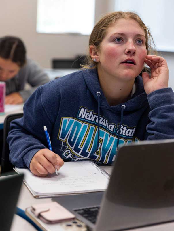 A student in class sitting at a table with notes in front of her. She's looking up toward the instructor.
