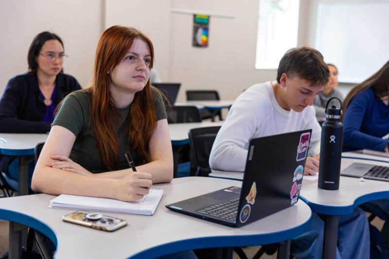 students in class sitting at tables with notes in front of them