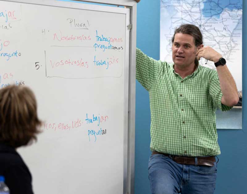 Ian Caldon speaking to a student in front of a white board with Spanish word written on it.