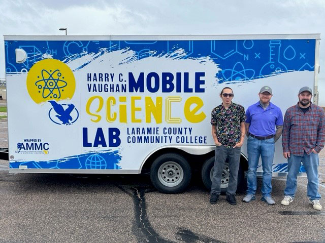 Photo of the STEM mobile lab with three students standing in front of it.