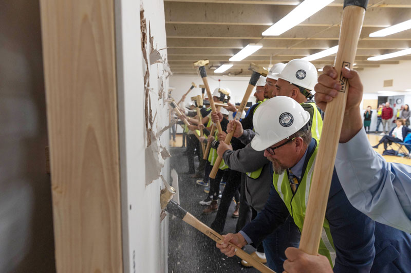 Photo of the ground breaking ceremony for the RAC with a group of people hitting a wall with sledge hammers.