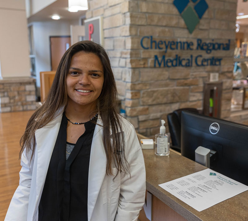 Thalita Portela in a white coat in front of a sign for Cheyenne Regional Medical Center