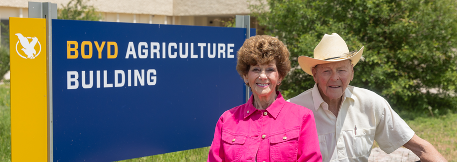 Rogene and Bob Boyd sitting in front of the sign for the Boyd Ag Building on campus