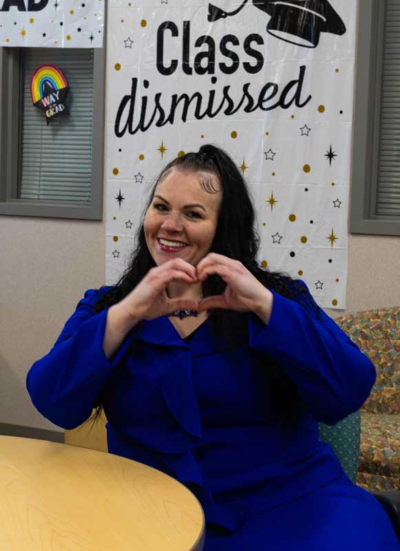 Jennifer Lamblin sitting at a table in the Business Building with a class dismissed sign behind her