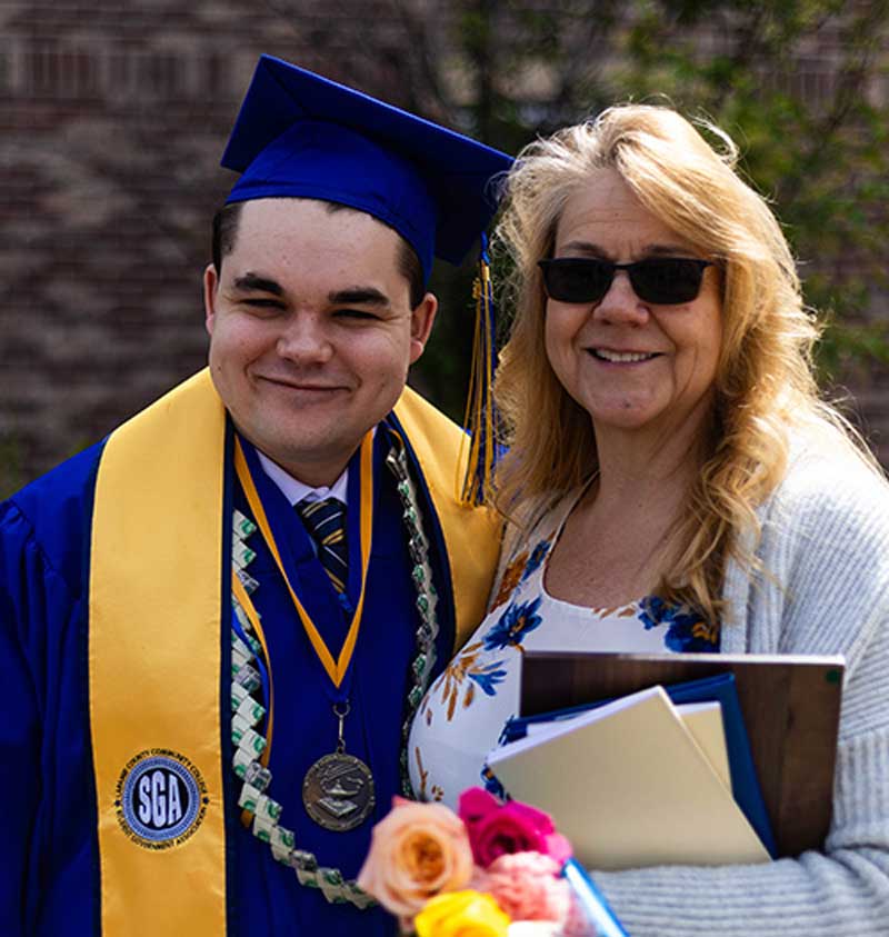 Caius Krupp standing with his mom after the graduation ceremony in his cap and gown