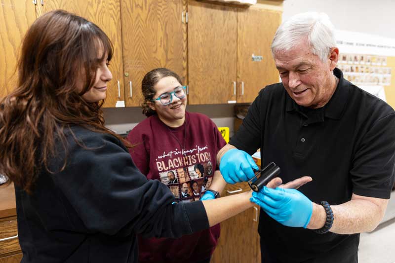 Donnie Heiduck shows students how to take hand prints with ink on a roll in class