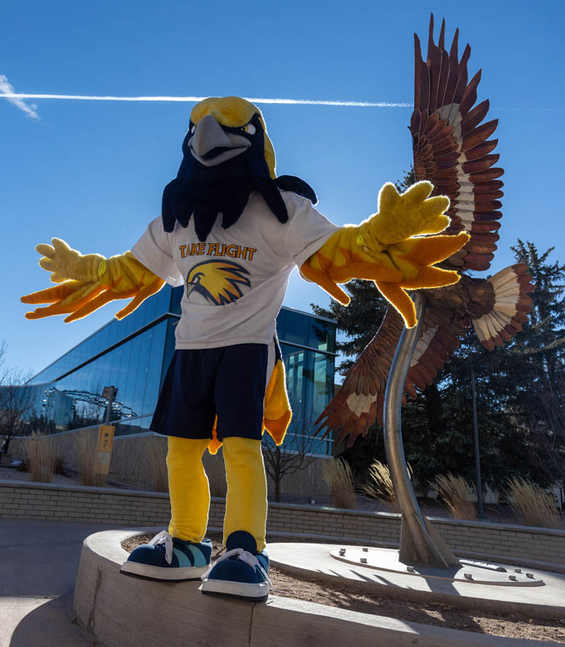 Talon the mascot standing near an eagle scuplture on campus
