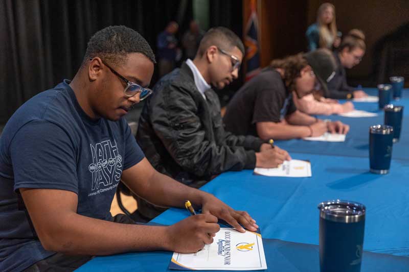 students lined up at a table signing a certificate to attend LCCC