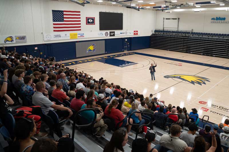 students and family sitting in the LCCC gym listening to the LCCC president at the start of The Kickoff event