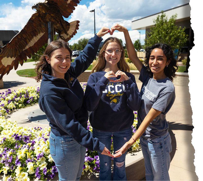 Three LCCC students standing in front of the Eagle statue making hearts with their hands.