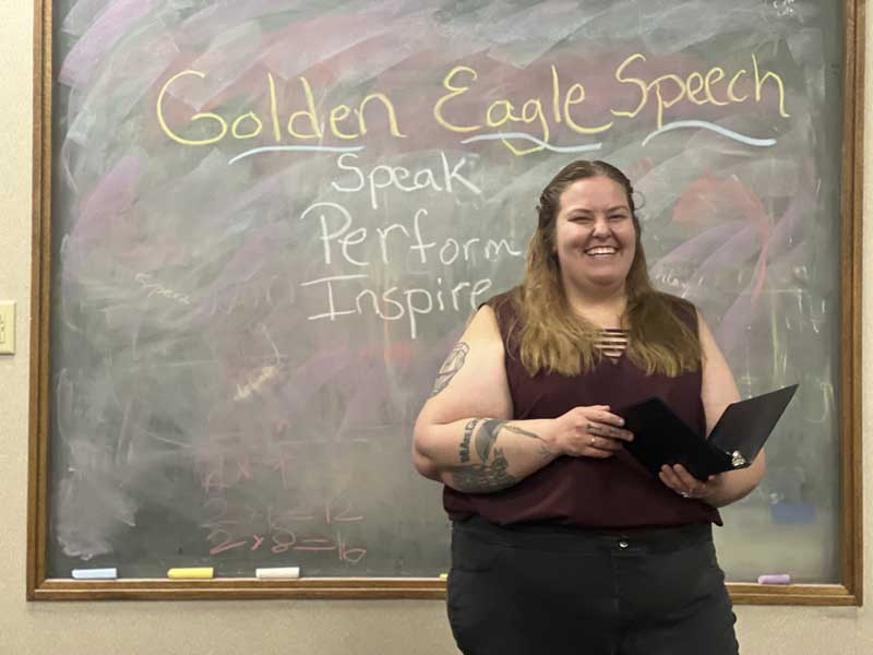 A speech student standing in front of a chalkboard with a notebook while speaking