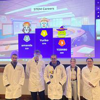 Students dressed in lab coats in front of a screen at Trivia night