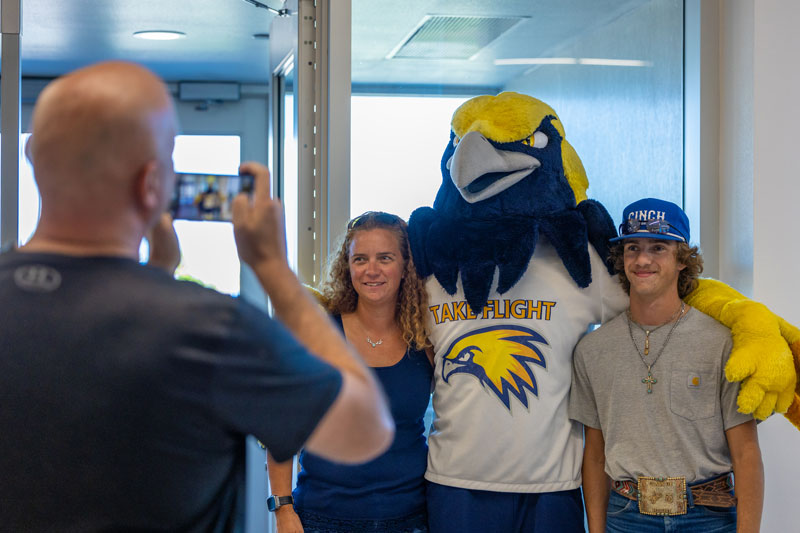  A person taking a photo of two people posing with the mascot Talon