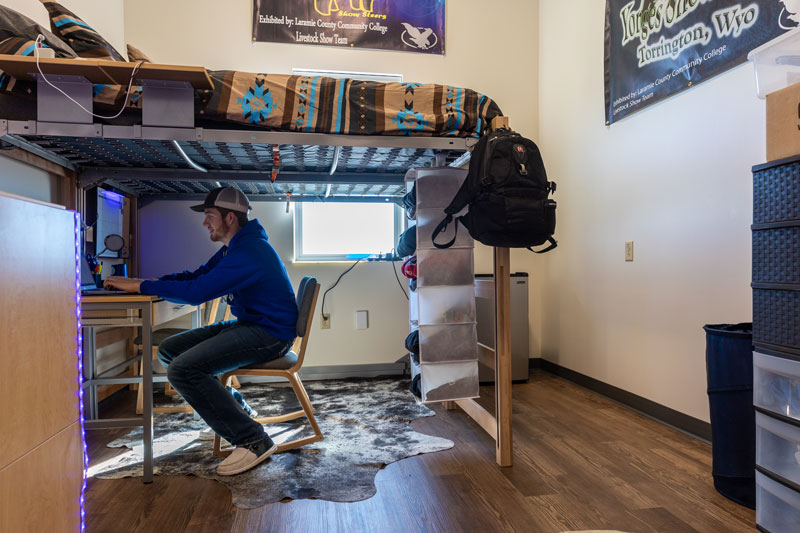 Photo of a student sitting in his dorm room under his lofted bed at a desk.
