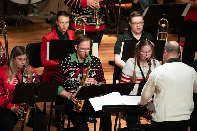 musicians playing saxaphones on stage during a concert in holiday sweaters