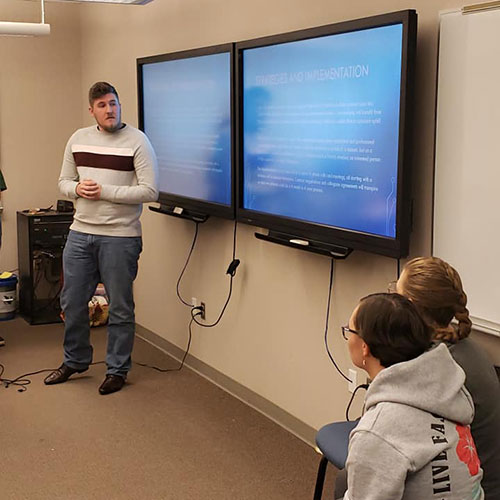 student standing near smart board giving presentation to class