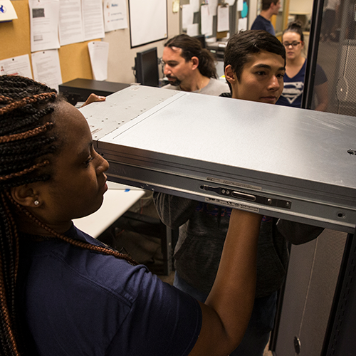 two students putting a server on the rack in a classroom