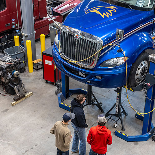 three students standing under a diesel truck looking up in the diesel shop