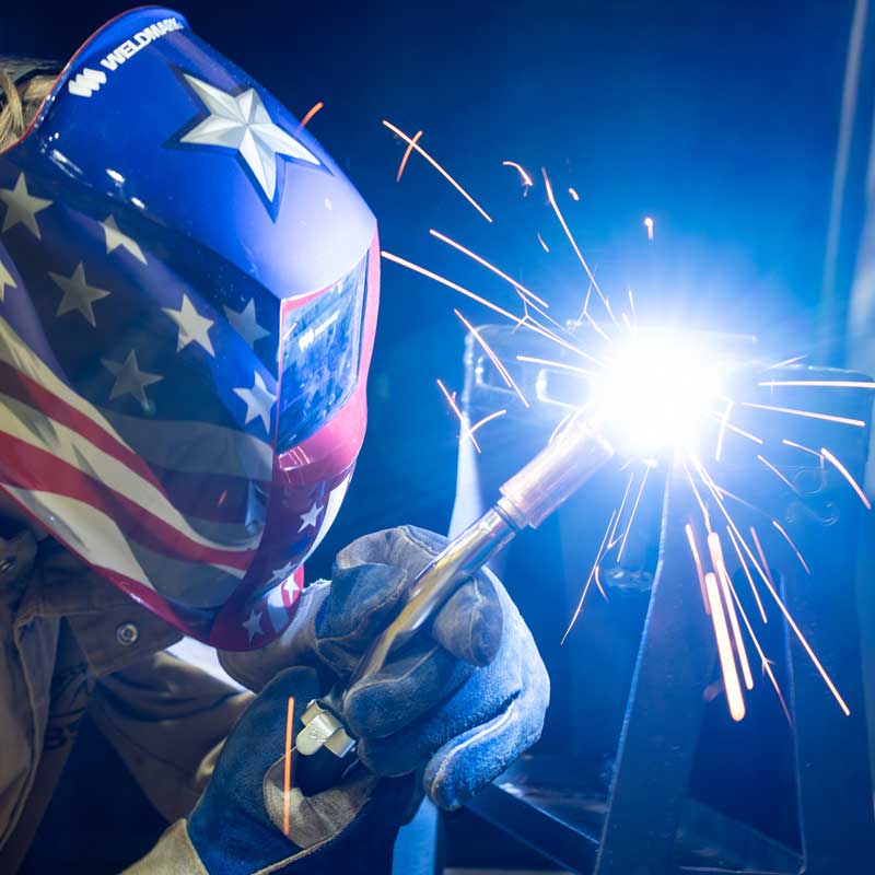 student welding in a helmet with a flag graphic on it