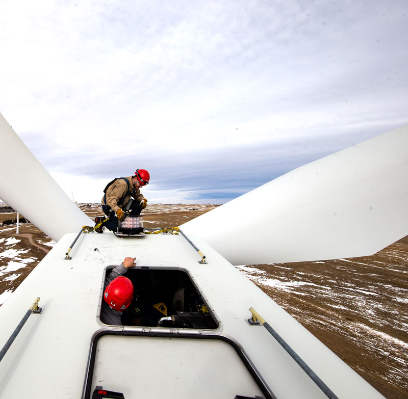 wind energy student on top of a wind turbine with instructor sticking head out of door talking