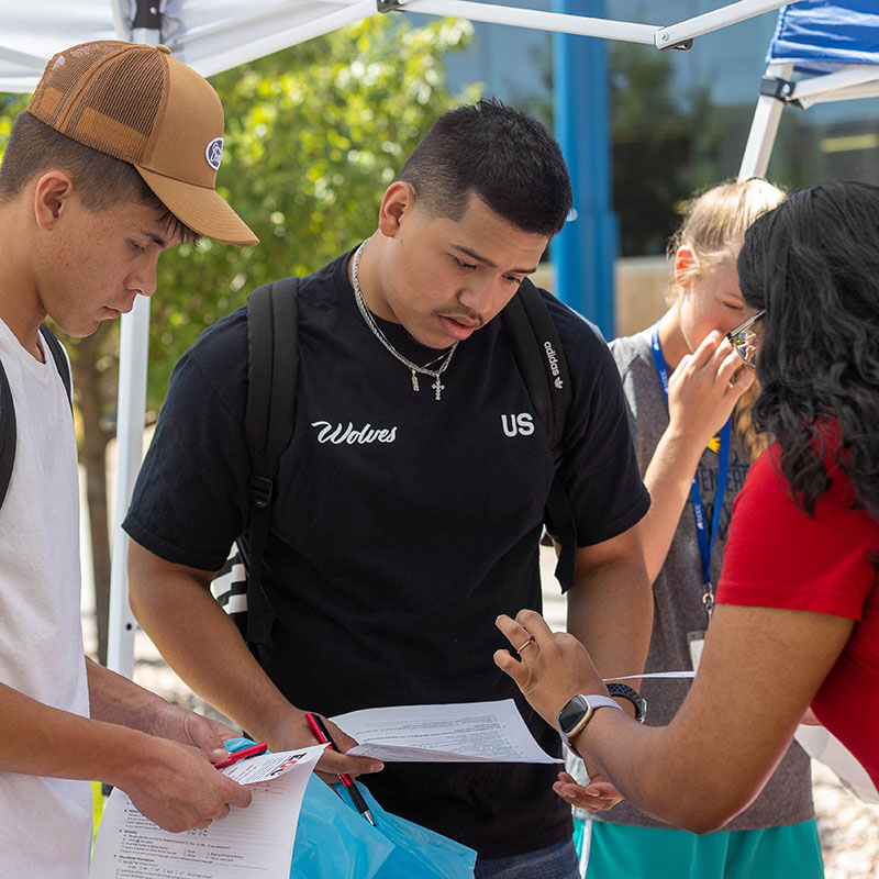 two students talking with a faculty member at a Campus Resource fair booth
