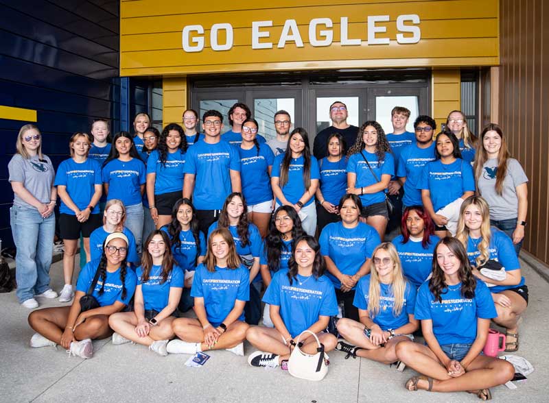 Group photo of the 2025 Davis First Generation Experience participants wearing matching program t-shirts in front of the entrance to the RAC where it says "Go Eagles"